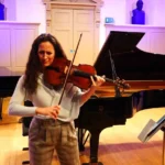 York Bowen: Φωτογραφία γυναίκας που παίζει Βιόλα μπροστά από ένα πιάνο, κλασική μουσική.